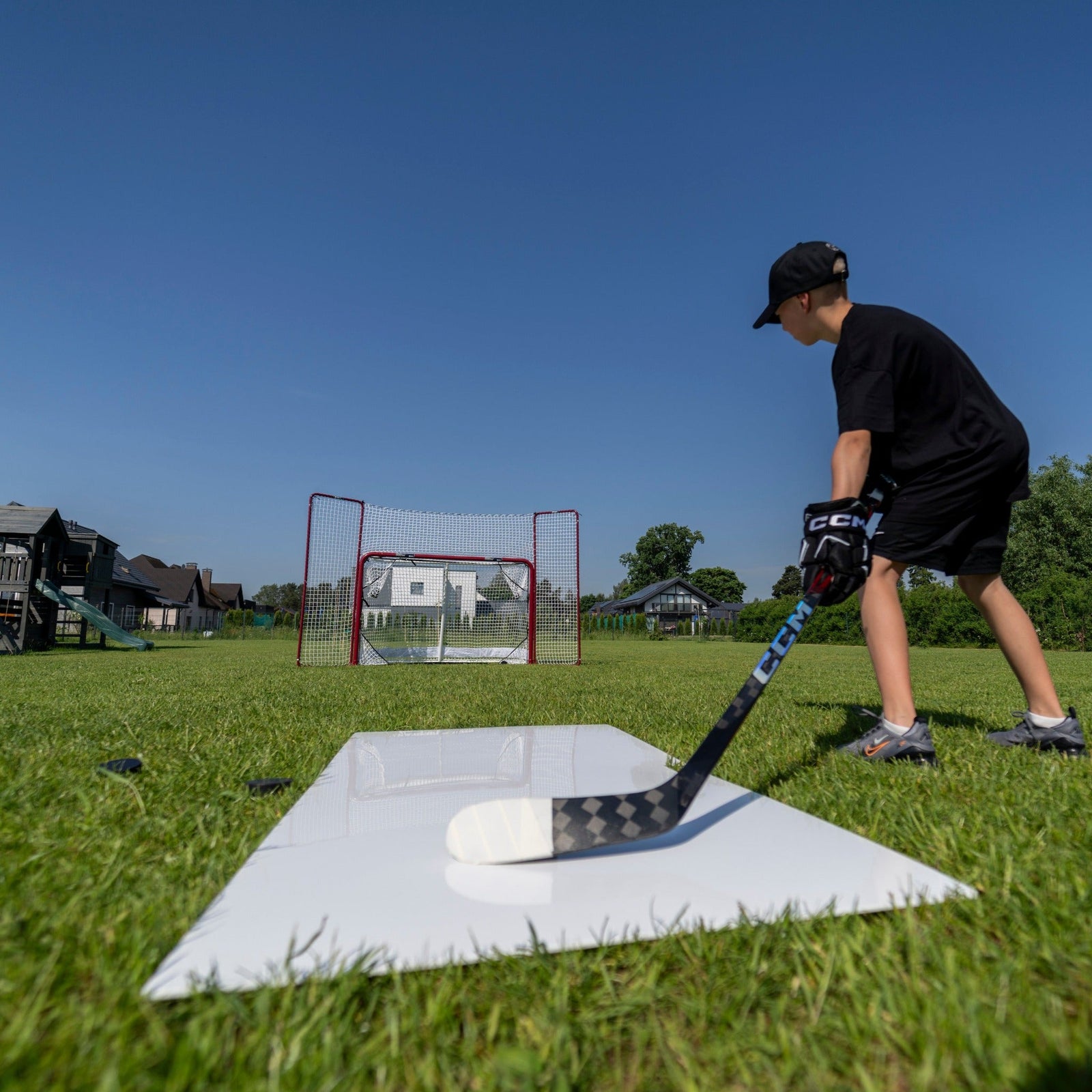 Young hockey player shooting from a pro shooting pad toward a net in the backyard