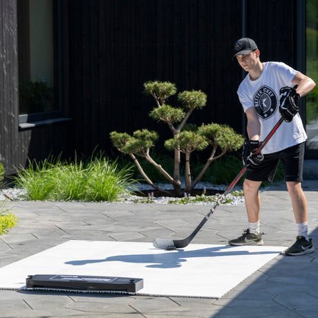 Young hockey player training with a stick and puck on interlocking tiles in a backyard