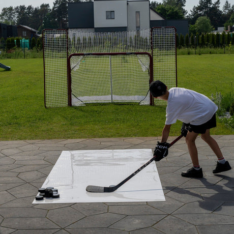 Young hockey player shooting pucks from a roll-up shooting pad toward a net in the backyard