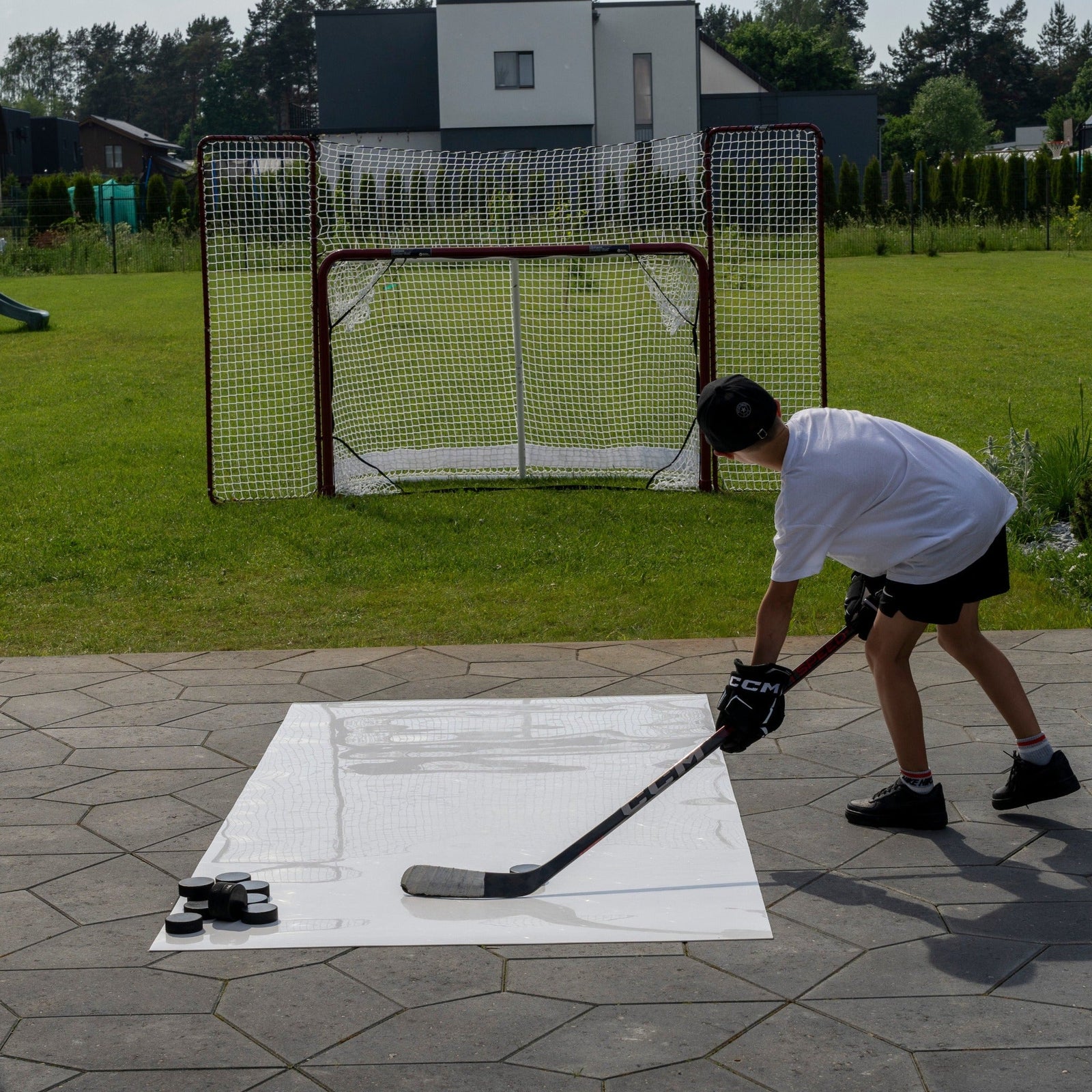Young player practicing hockey shooting at home from a roll-up shooting pad toward a net with backstop