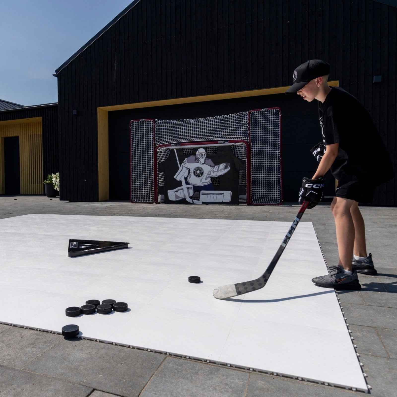 Young player stickhandling a puck on hockey flooring tiles in a home driveway rink