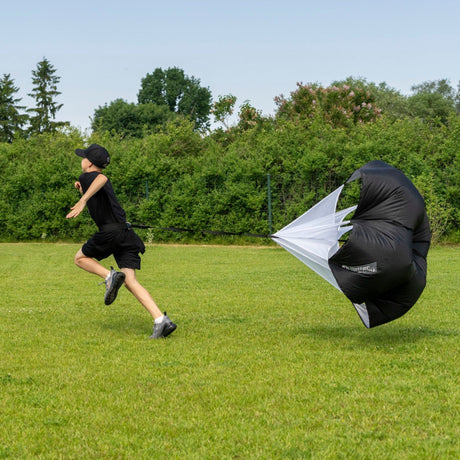 Young hockey player sprinting with a resistance speed chute in a backyard for off-season training