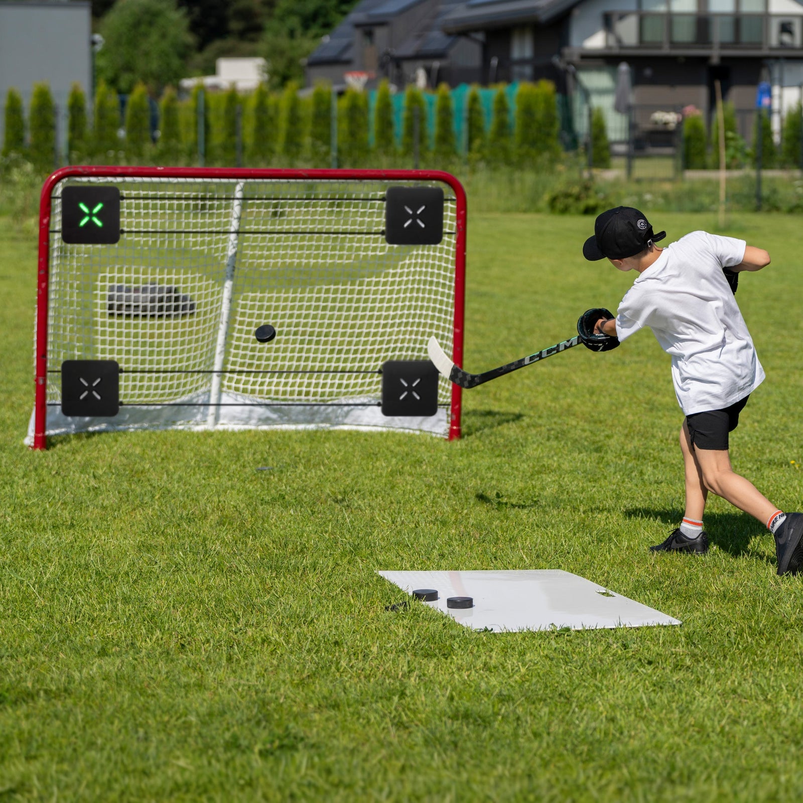 Young hockey player training shooting accuracy in the backyard with corner targets in the net