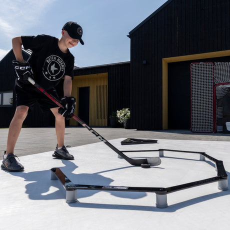 Young hockey player training heads-up stickhandling outdoors with a stickhandling trainer on a driveway